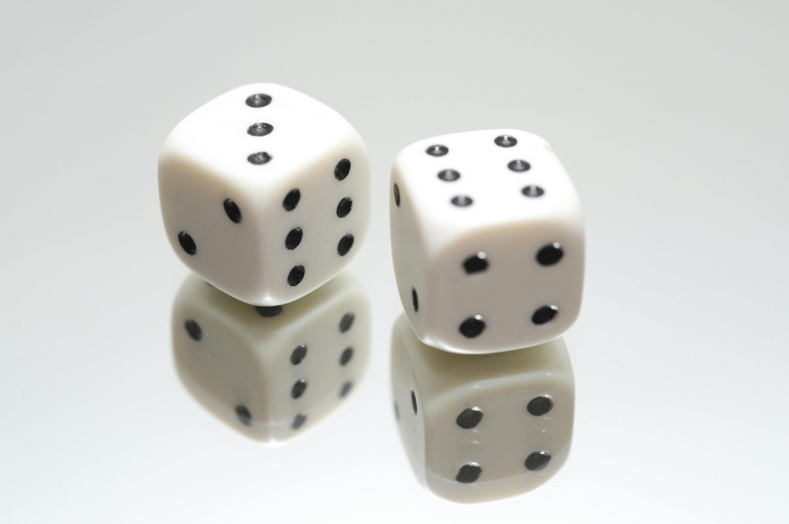 A close-up view of two white dice with reflection on a smooth white surface, symbolizing luck and chance.