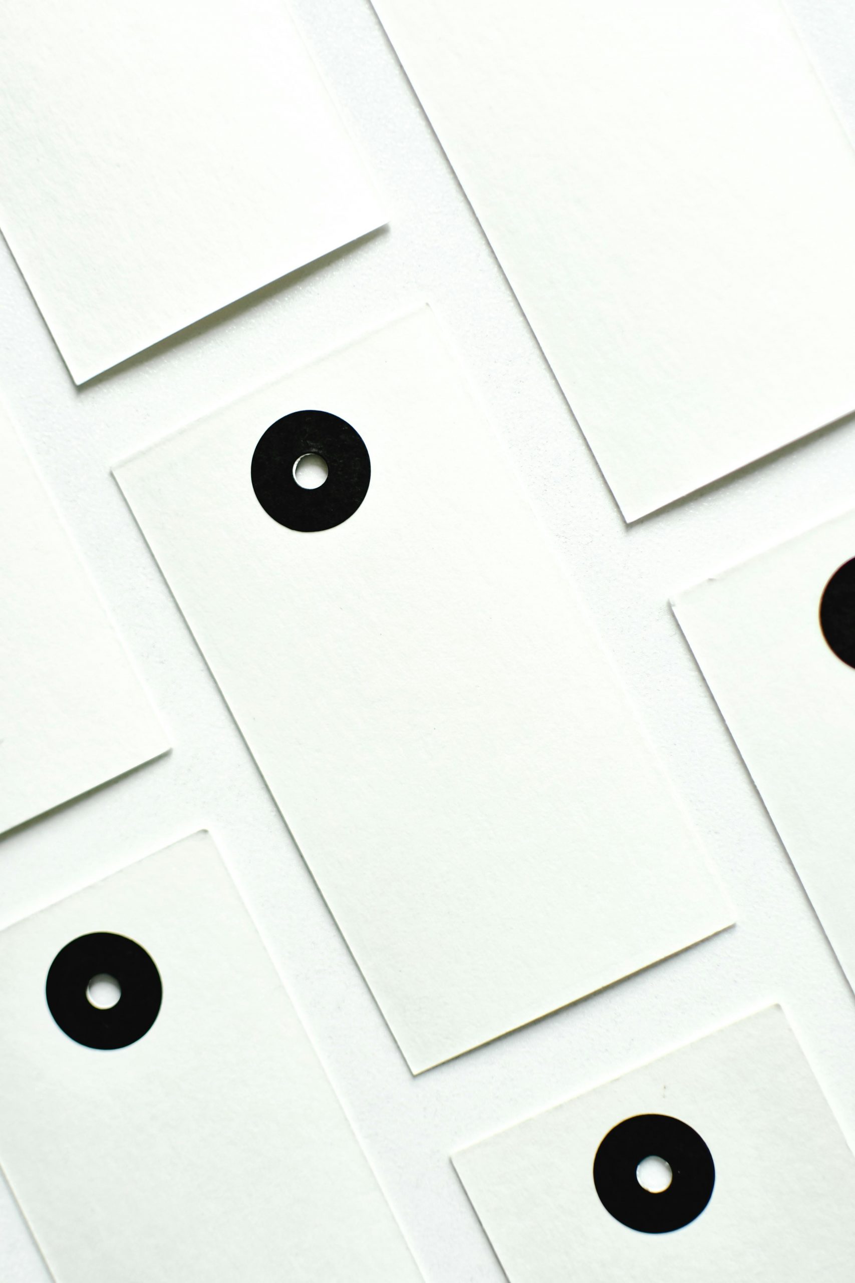 Abstract minimalist composition featuring white tags with black eyelets arranged on a white background.